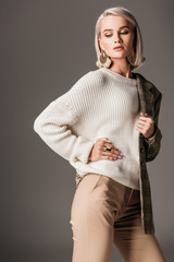 fashionable girl posing in white sweater and tweed jacket on one shoulder, on grey