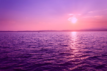 Beautiful purple sunset with floating boat on Lago di Garda near Scaliger Castle, Sirmione, Italy, romantic love concept