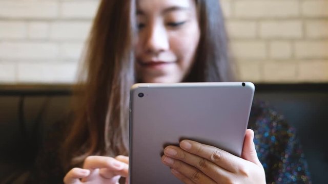 A beautiful Asian woman with smiley face holding , using and typing at tablet pc in modern cafe