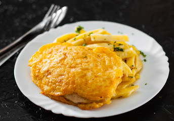 Fish and Chips. Fried fish fillet in cheese and potatoes in a white plate on black background.