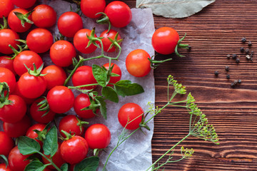 Small red cherry tomatoes spill out of a wicker basket on an old wooden table in rustic style, selective focus