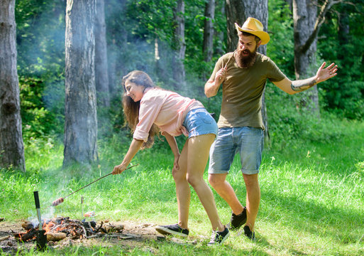 Man bearded hipster looks at sexy female buttocks. Seductive position. Girl bent down to fire while man enjoying sexy view. Couple picnic. Girl sexy buttocks denim shorts roasting sausage at bonfire