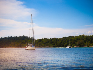 White sailboat in blue sea in sunny summer day with island view in background for vacation holiday...