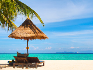 Wooden beach chairs and straw parasol on white sand beach with turquoise water sea and clear blue sky in sunny summer day at Koh Lipe island in Thailand for holiday or vacation concept.