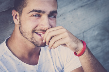 cheerful beautiful young boy teenager caucasian people sitting with a urban city wall in background. looking at the camera smiling in handsome style. blue eyes