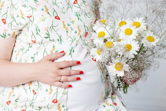 Closeup of pregnant woman holding flower and touching her belly
