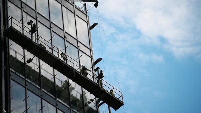 Construction workers on a suspended platform on a skyscraper glass facade