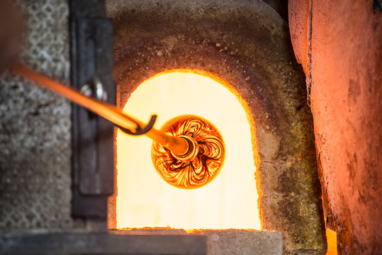 Fototapeta Murano glass-blowing factory. Glass blower forming beautiful piece of glass: put iron rod with attached glass object in furnace to make the glass malleable. Italy