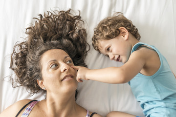 A woman and her son playing in bed.