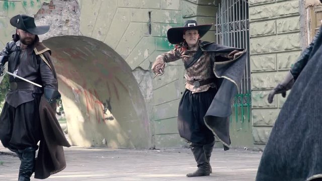 Two men fight against the musketeer in black clothes and push him with his foot