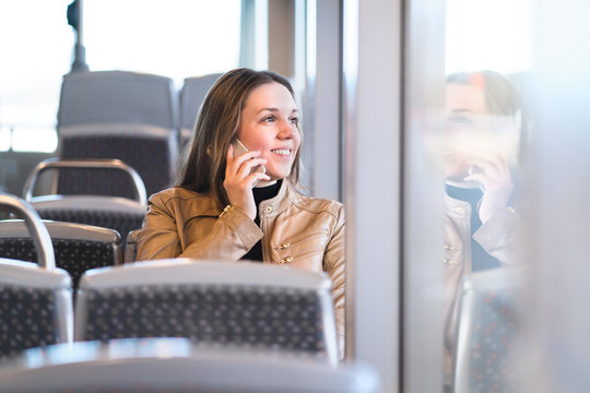 Woman Talking On The Phone While Riding The Bus, Train, Metro Or Subway. Happy Lady With Smartphone In Public Transportation Looking Out The Window.