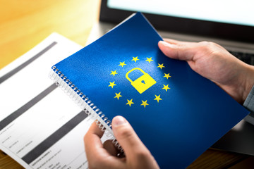 GDPR (General Data Protection Regulation) concept. Business man holding notebook with European Union (EU) flag logo and lock icon. Laptop computer and paper form on desk and table. - obrazy, fototapety, plakaty