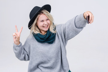 Happy cute woman making selfie over gray background. Wearing in bright scarf , sweater and hat. Looking at camera