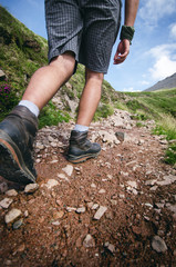 Man hiker walking on mountain rocks with sticks. Beautiful weather with Scotland nature. Detail of hiking boots on the difficult pathway, trail, Friends in the nature and enjoying sport.
