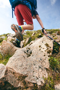 Man hiker walking on mountain rocks with sticks. Beautiful weather with Scotland nature. Detail of hiking boots on the difficult pathway, trail, Friends in the nature and enjoying sport.