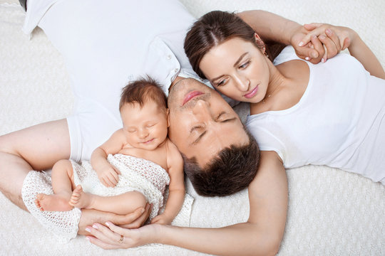 Parents cuddling newborn baby in bed at home. Mom, dad and baby.  Happy family concept