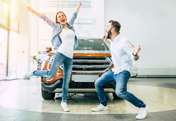 The successful visit to the dealership. Happy young couple chooses and buying a new car for the family. - obrazy, fototapety, plakaty
