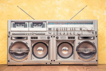 Retro outdated portable stereo boombox radio receiver with cassette recorder from circa 80s front concrete textured yellow wall background. Listening music concept. Vintage old style filtered photo