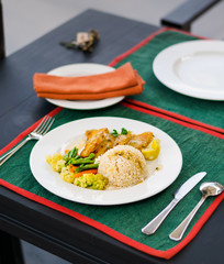 Lunch dish with rice ball, greens and fried fish with gravy, in a white plate, on a restaurant terrace.