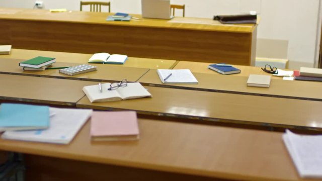 Tracking shot of empty lecture theater at university with notebooks and school supplies left on desks