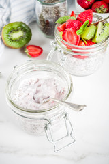 Healthy dietary vegan breakfast, yoghurt with chia seeds and fresh fruits, strawberries, kiwi.White marble background copy space