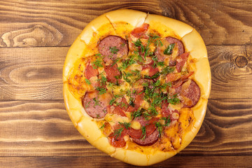 Homemade delicious pizza with salami, tomatoes and dill on wooden table. Top view