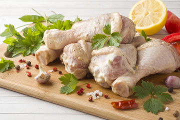 Raw chicken drumstick in marinade with sauce, pepper and greens on wooden stand. Selective focus