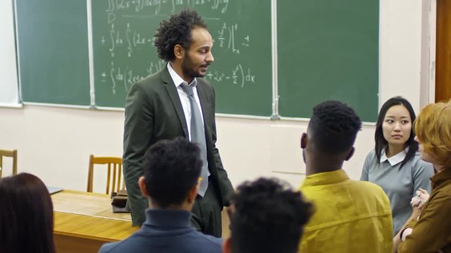 Handheld shot of middle-aged teacher of mathematics talking to multi ethnic group of students standing around him and answering their questions after lecture on calculus