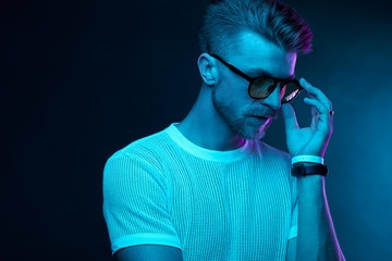 Neon light studio portrait of attractive male model with mustaches and beard in sunglasses and white t-shirt