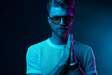 Neon light studio portrait of attractive male model in sunglasses and white t-shirt
