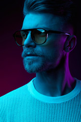 Neon light studio portrait of serious man model with mustaches and beard in sunglasses and white t-shirt