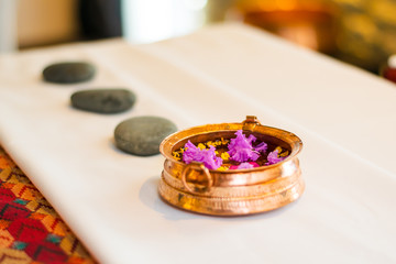 Folded massage towel, flower petals, pebble stones and copper pot on a massage bed in a luxury resort spa, Nepal.