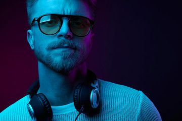 Neon light portrait of smiling man with headphones on neck,in sunglasses and white t-shirt.