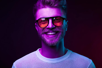 Neon light portrait of smiling man model with mustaches and beard in orange sunglasses and white t-shirt - 216136648