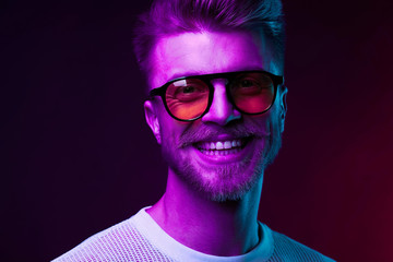 Neon light portrait of smiling man model with mustaches and beard in orange sunglasses and white t-shirt