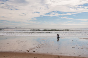The coast of the Atlantic Ocean at low tide and a pair of elderly people strolling along the sand. USA. Maine.
