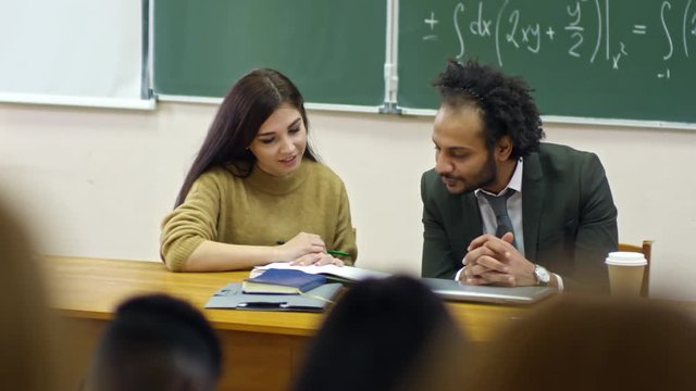 Medium shot of pretty young female student showing work to male professor and asking questions during mathematics class