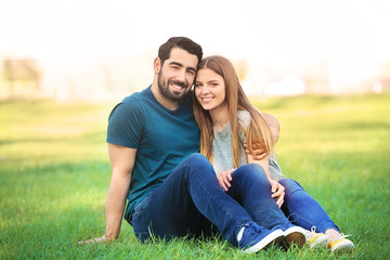 Happy young couple sitting on green lawn in park