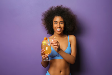 Naklejka premium Beautiful African-American woman in bikini and with tasty cocktail on color background