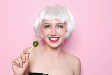 Young woman with wig and lollipop on color background