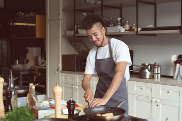 Young African-American man cutting vegetables in restaurant kitchen during cooking classes