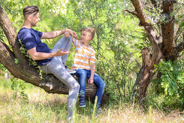 Naklejka na ściany i meble Little boy and his dad sitting on tree outdoors