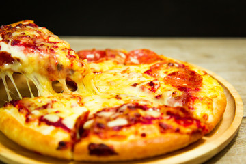 Very cheesy pizza slice in hand.Hot pizza slice with melting cheese on a rustic wooden table.