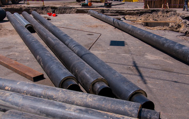 Big black dusty pipes lying on the asphalt next to the hole. Concept of repairing and changing a...