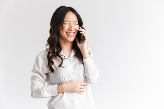Image of brunette chinese woman with long dark hair holding and talking on cell phone, isolated over white background in studio