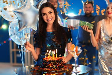 Young woman near her birthday cake at party in club