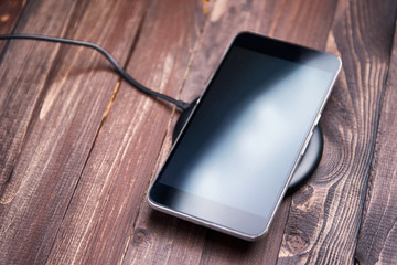 Mobile phone lies on a wireless charger on a wooden brown background © jalisko