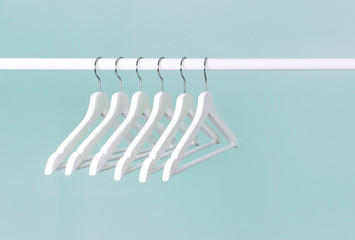 Many wooden white hangers on a rod, isolated on blue turquoise wall background. Store concept, sale, design, empty hanger. Place for text. Soft focus. - obrazy, fototapety, plakaty