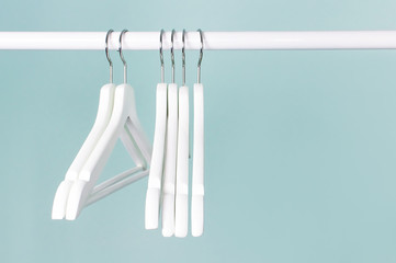 Many wooden white hangers on a rod, isolated on blue turquoise wall background. Store concept,...
