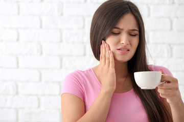 Young woman with sensitive teeth and cup of hot coffee on blurred  background - obrazy, fototapety, plakaty